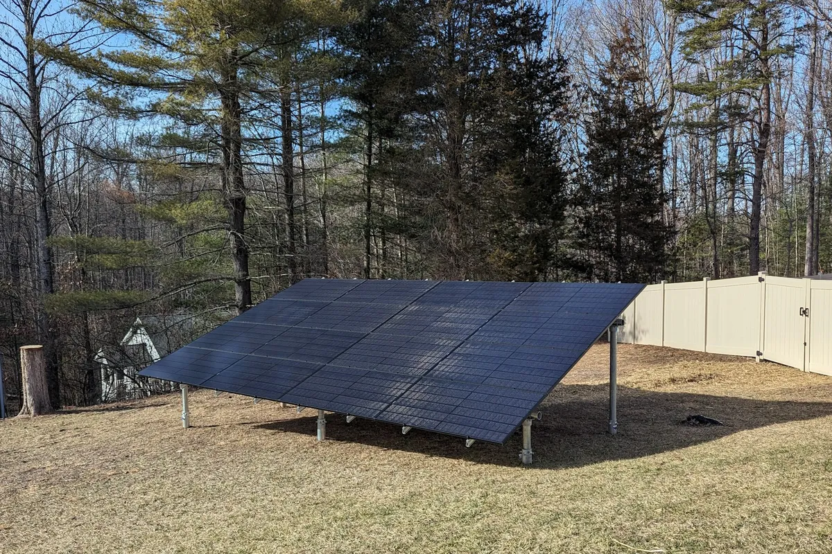 An all-black residential ground-mounted solar array on a green lawn