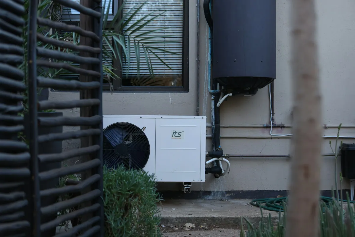 Split heat pump water heater with an outdoor compressor unit below a wall-mounted tank
