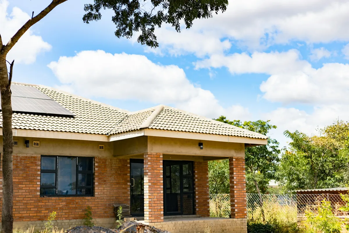 Brick house with a tiled roof and a few solar panels in the upper left corner under a blue sky