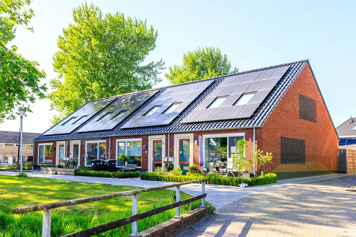 Brick house with dark solar panels on its sloped roof beside a lawn