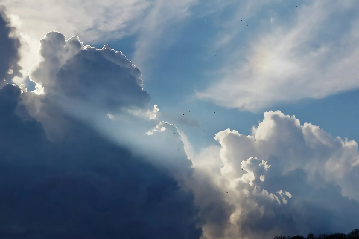 Large white and dark storm clouds with a beam of sunlight breaking through against a blue sky