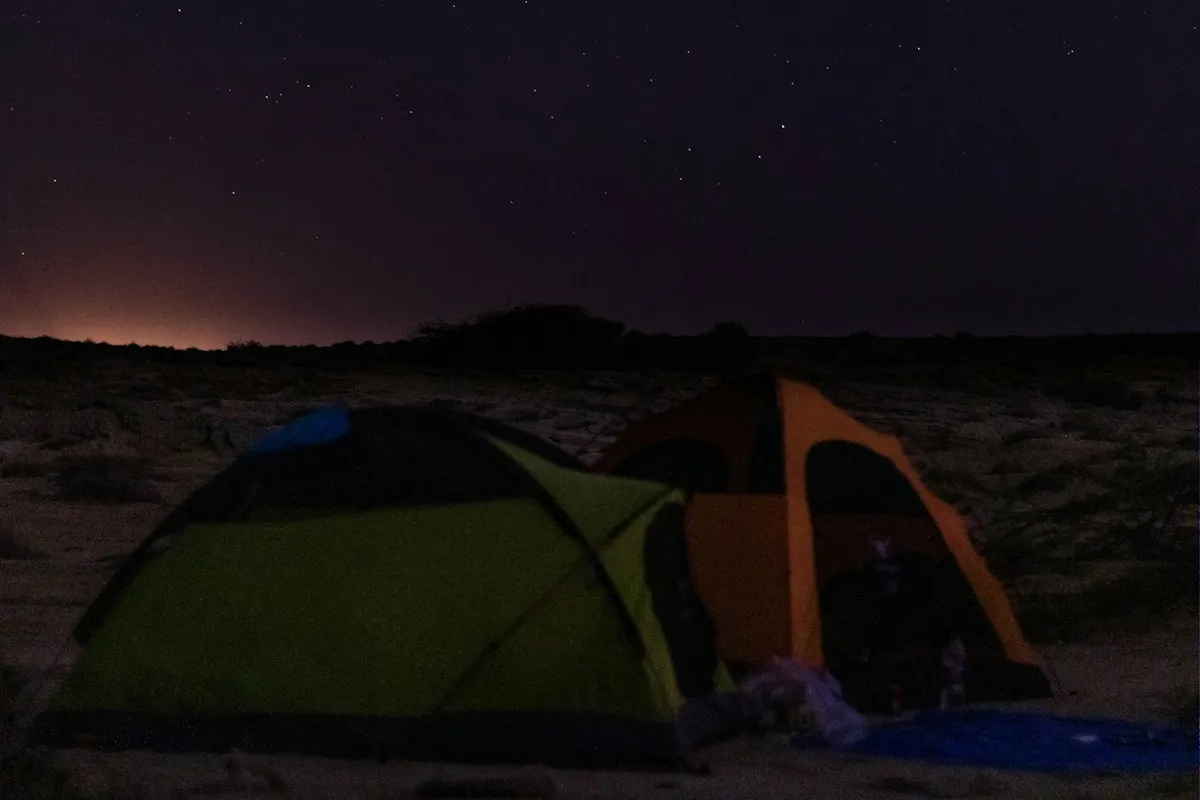 A tent glowing under a starry night sky at an off-grid campsite