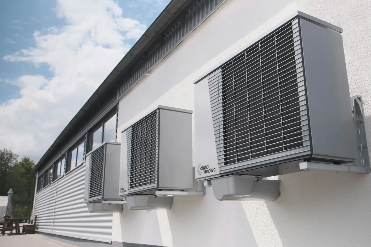 Three grey air conditioning units mounted in a row on a white wall