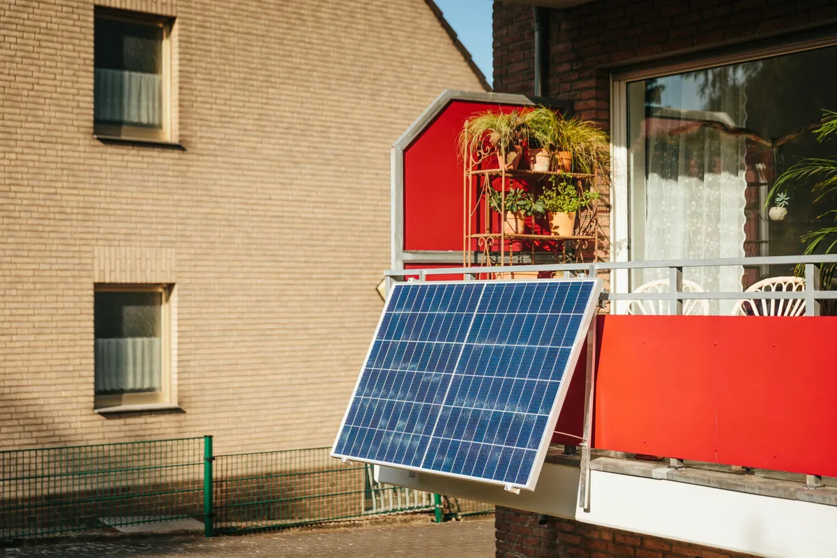 Balcony solar panel angled off a railing beside potted plants on an apartment terrace
