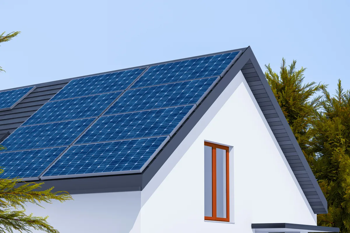 Solar panels covering the pitched roof of a white house against a clear sky