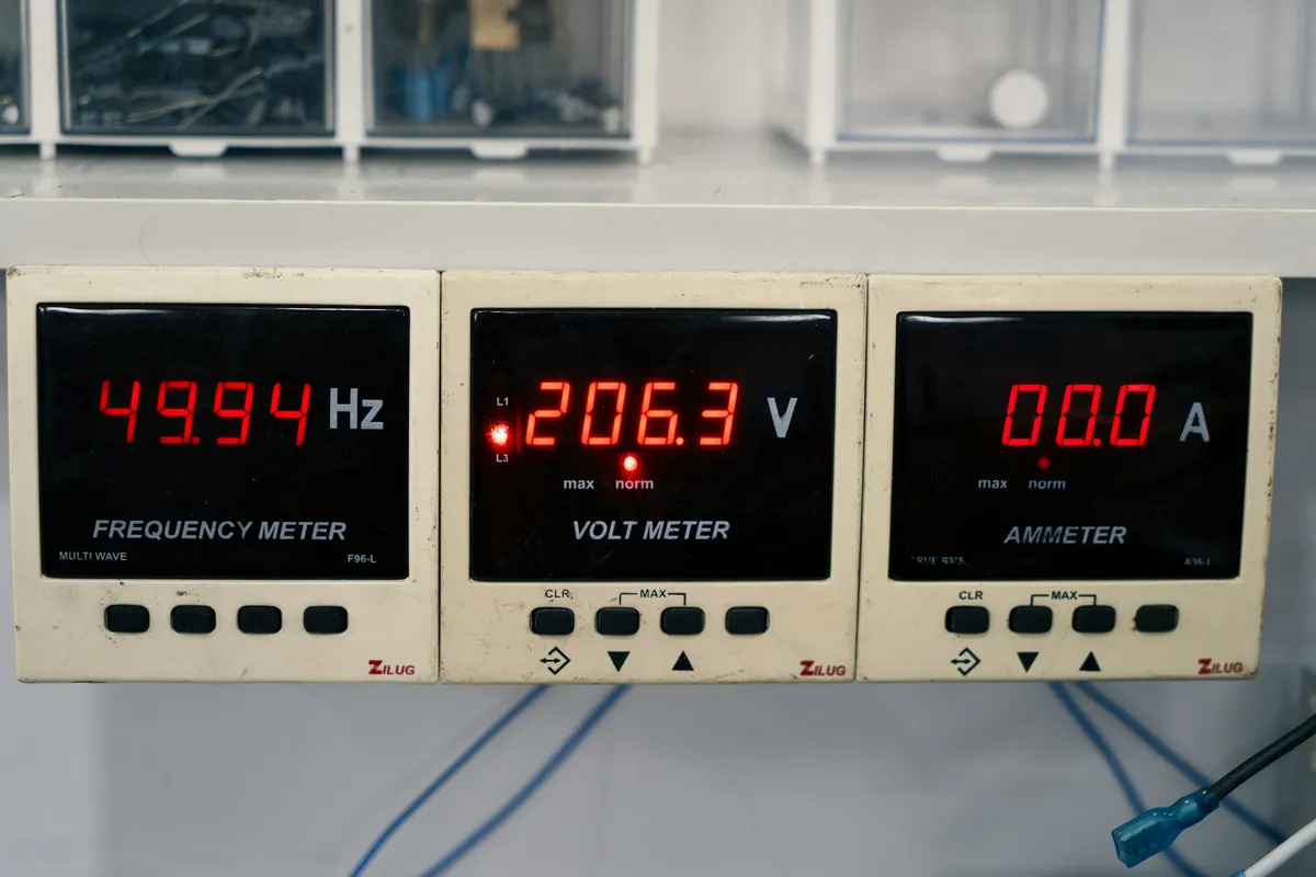 Three red-digit panel meters side by side showing frequency, voltage and current readings