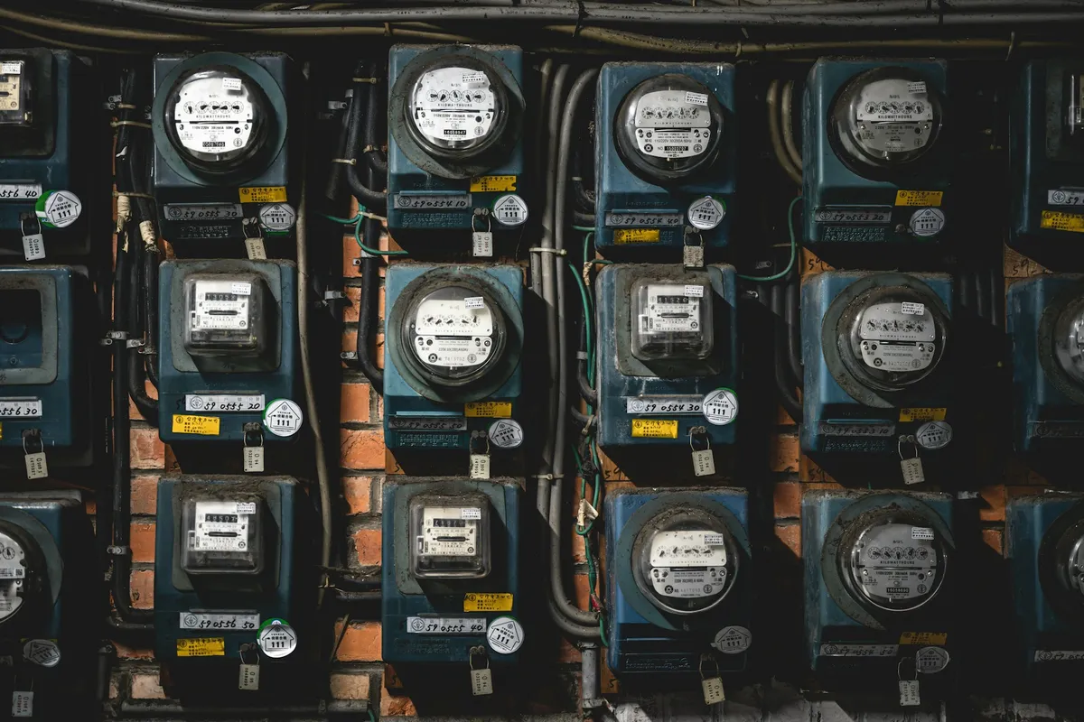 Rows of analog electricity meters with round dials mounted on a metering room wall