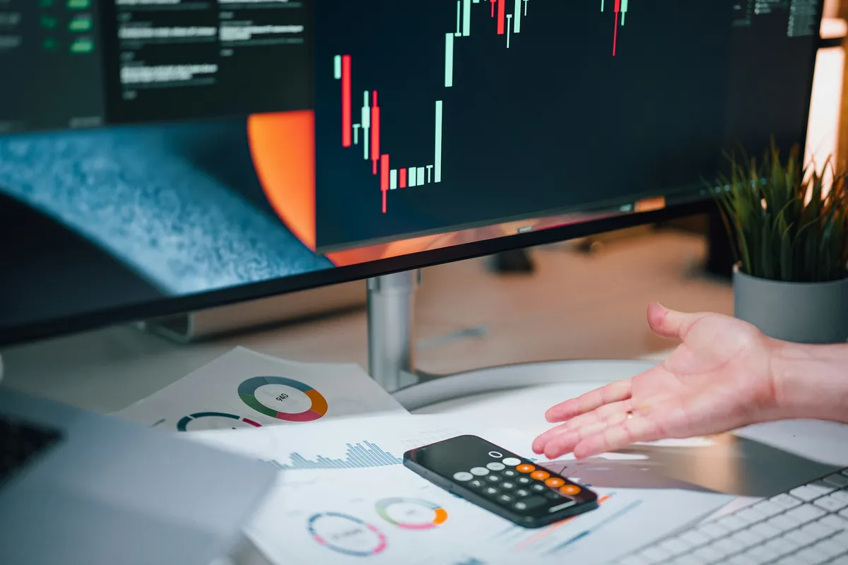 Hand resting beside a calculator on a desk covered with printed charts