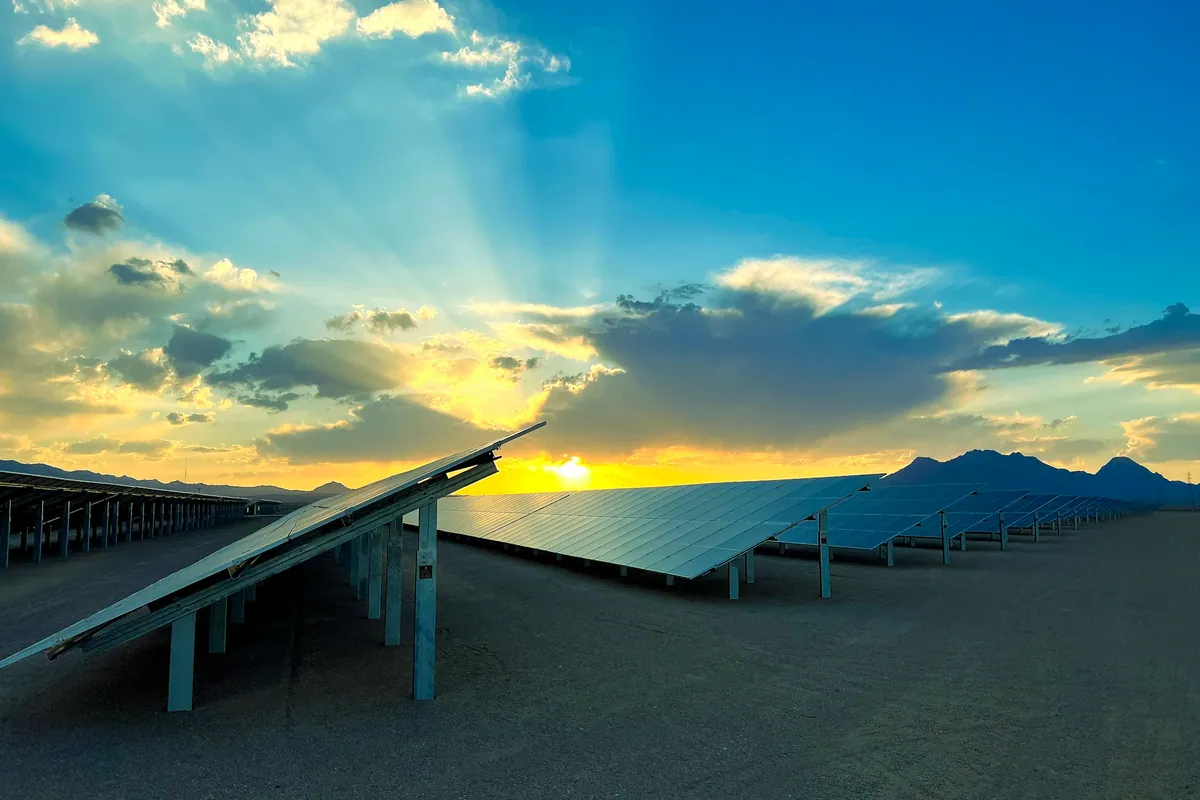Rows of ground-mounted solar panels at sunrise with sun rays breaking through the clouds