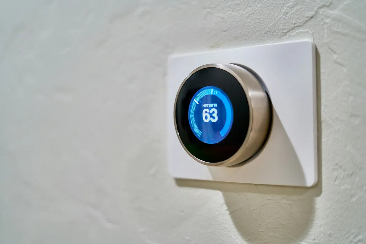 Wall-mounted smart thermostat showing 63 degrees on a white plaster wall