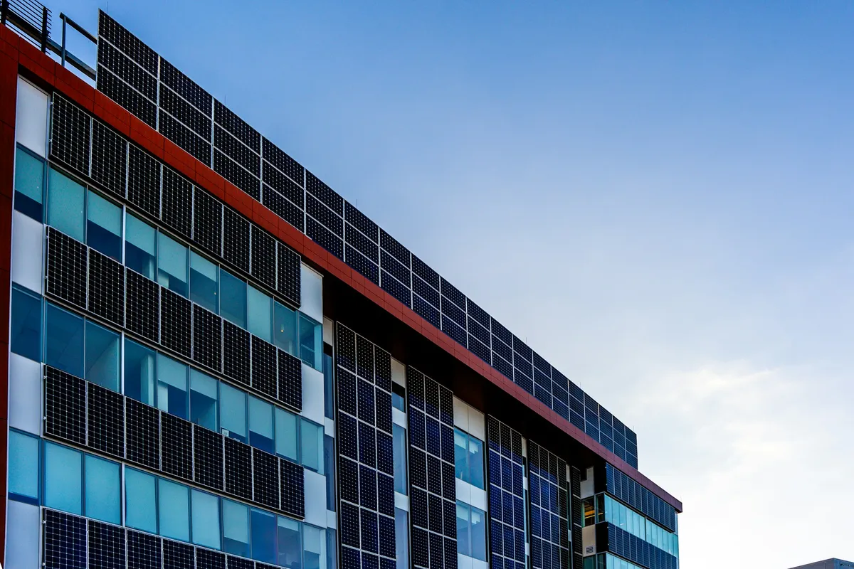 Office building facade and roofline covered in rows of dark solar panels under a blue sky