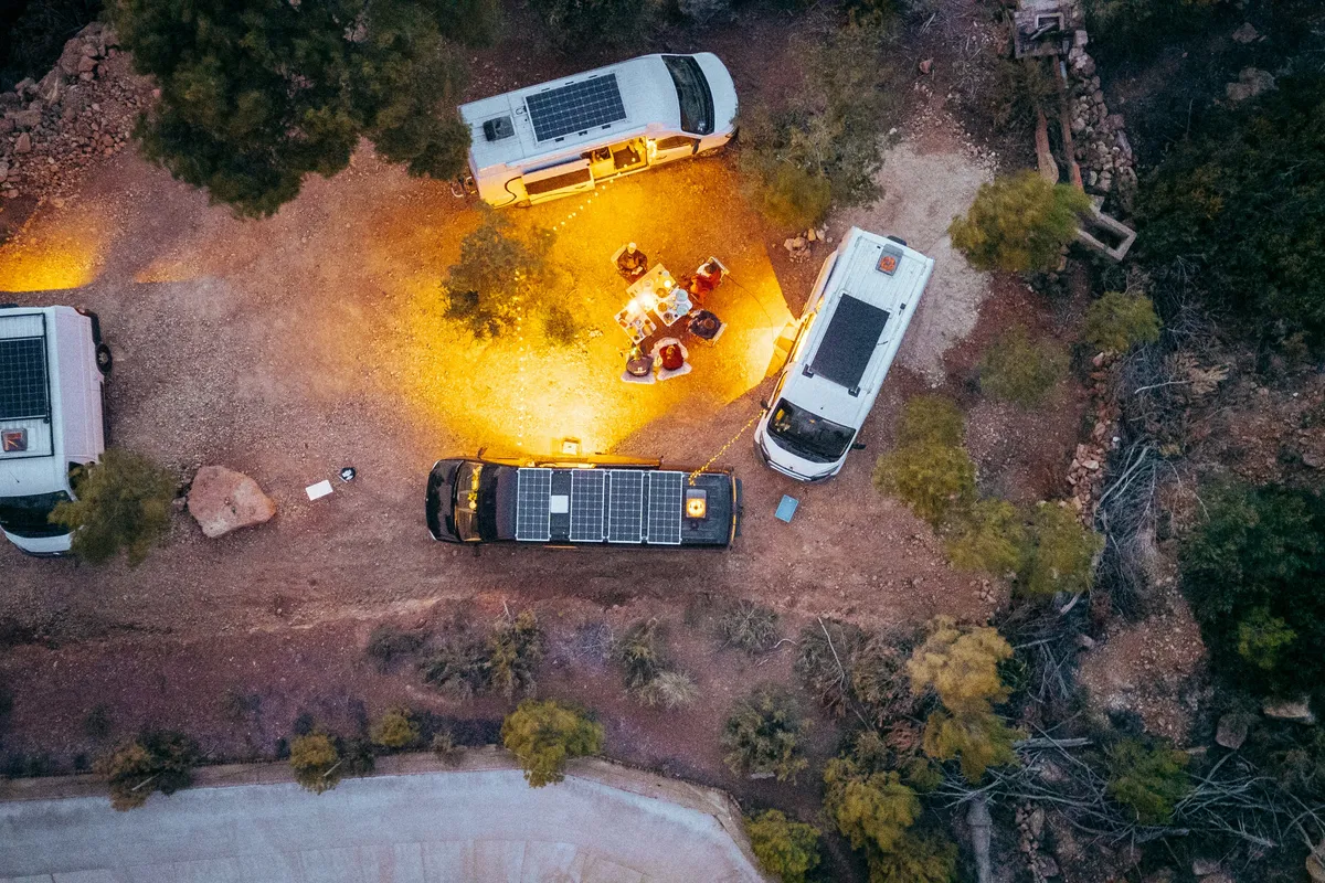 Aerial view of camper vans with roof solar panels around a glowing campfire