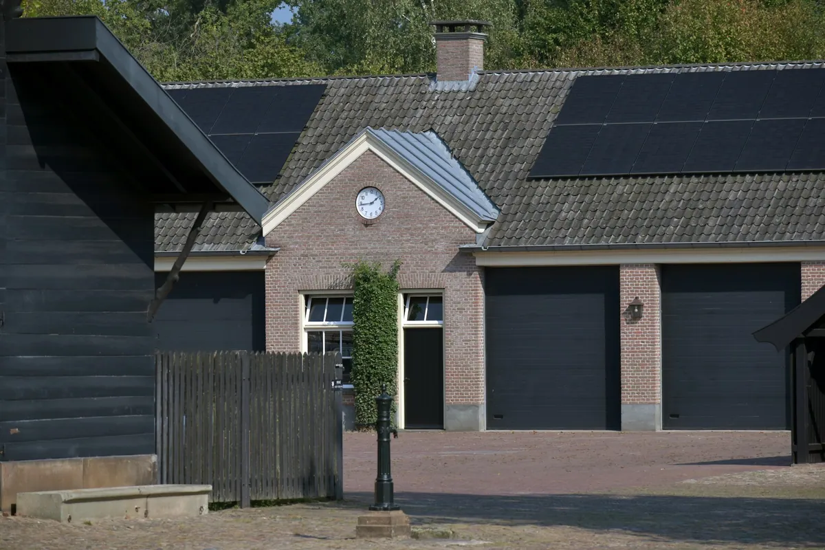 Brick building with a tiled roof and black solar panels on one slope, next to a dark timber barn