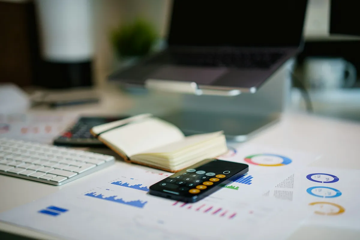 An office desk with a phone and printed financial charts and cost calculations