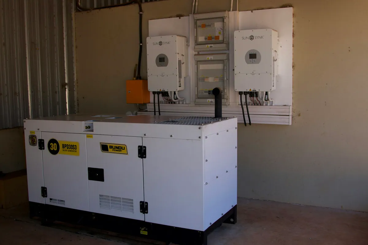 Two wall-mounted solar inverters above a white backup generator in a utility room
