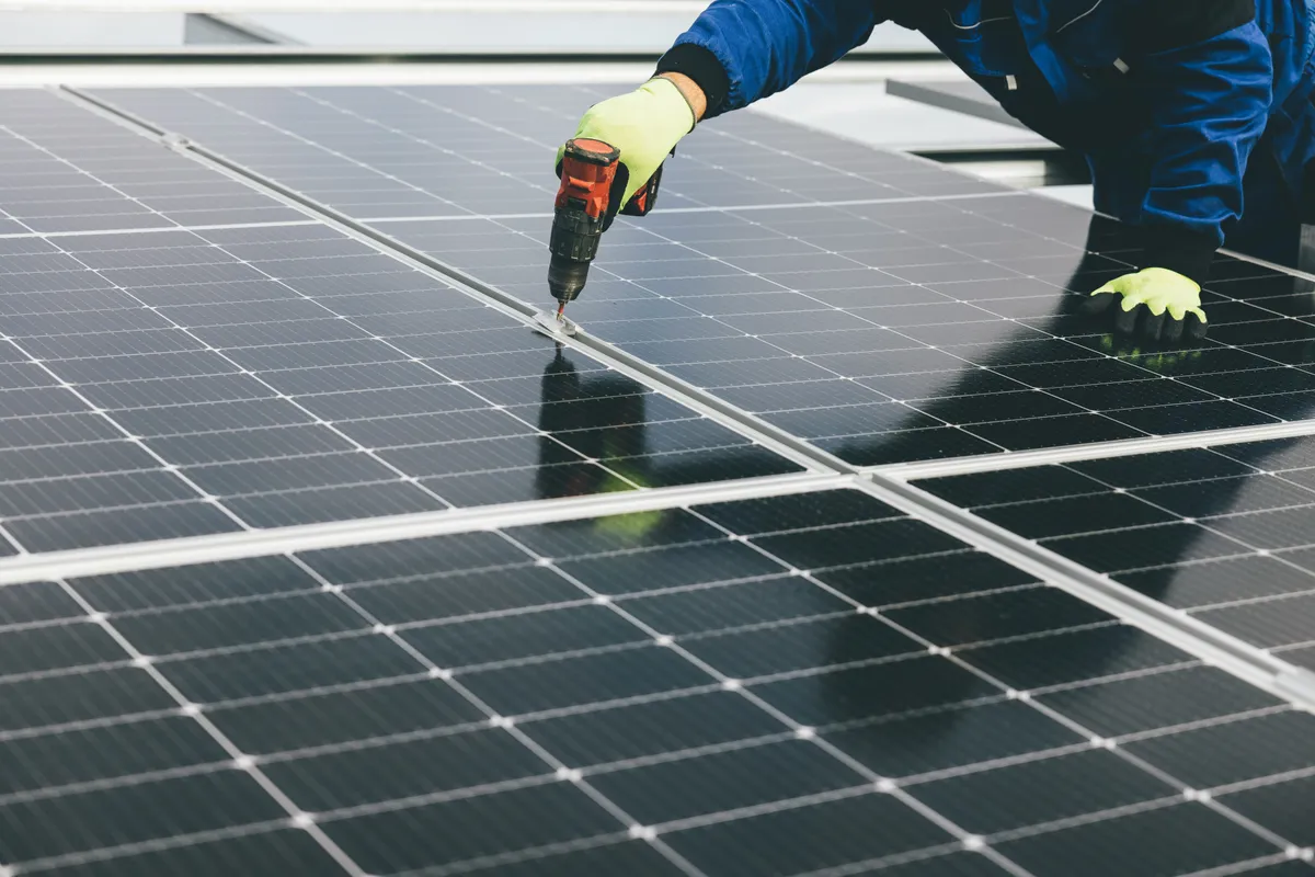 Technician using a cordless drill to service a large rooftop solar panel array