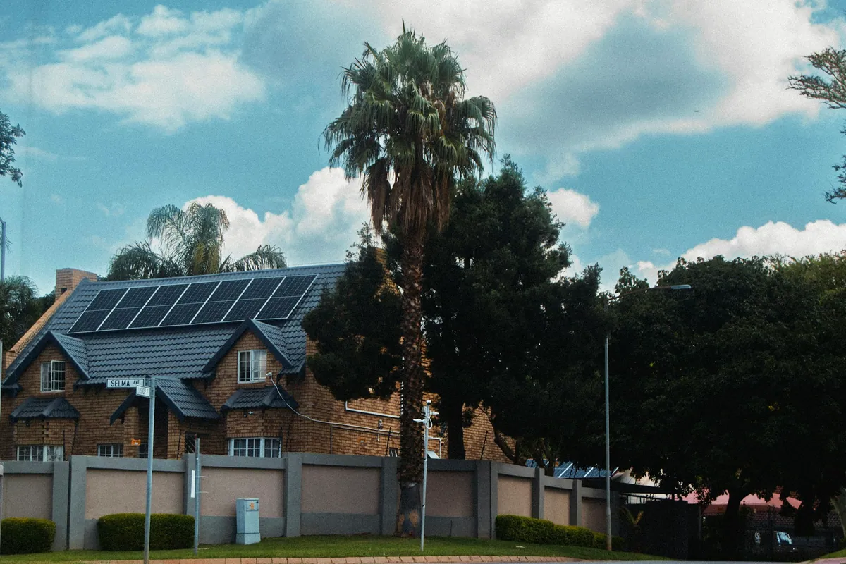 House with a rooftop solar array behind a palm tree on a suburban street corner