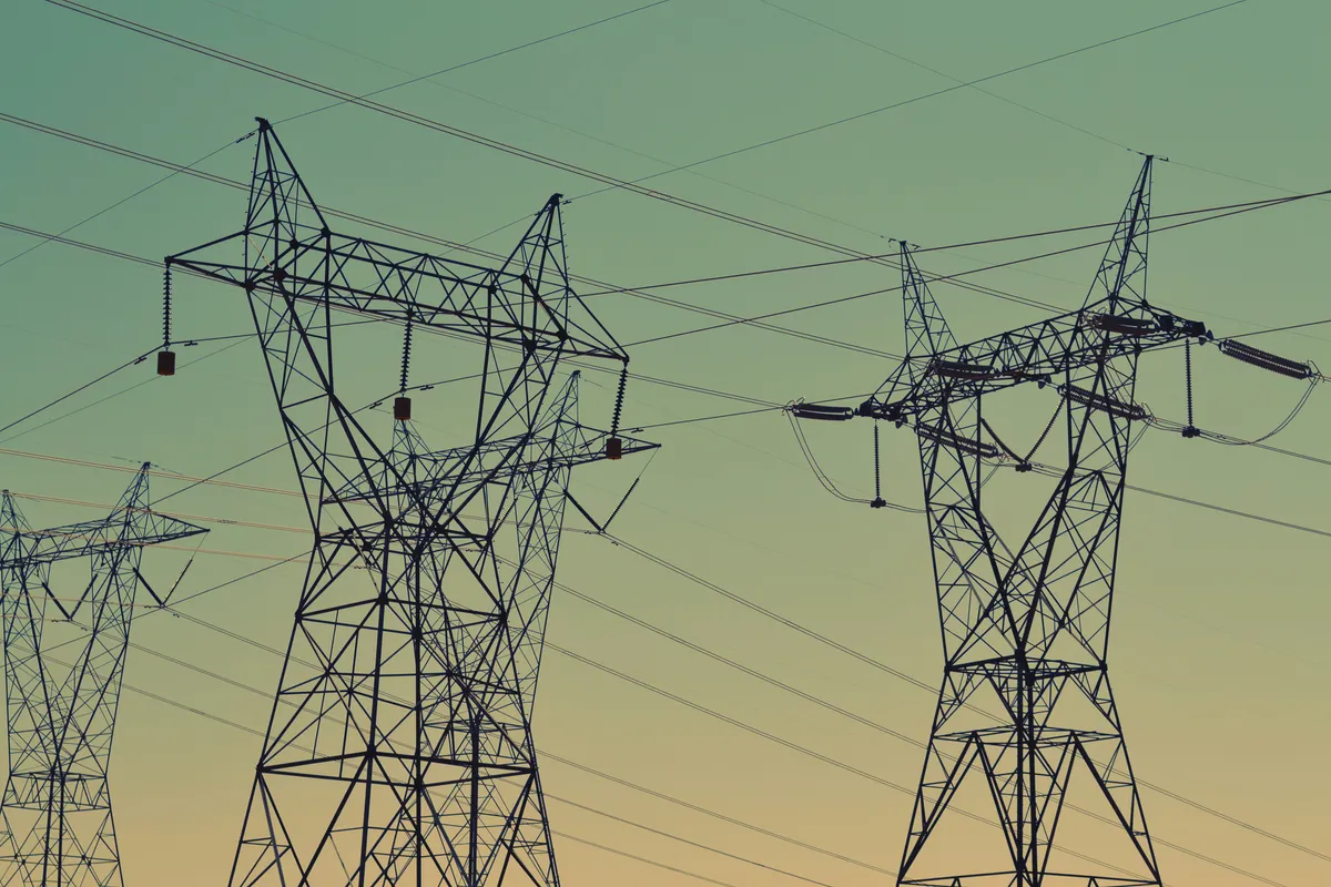 High-voltage transmission towers and power lines silhouetted against a green dusk sky