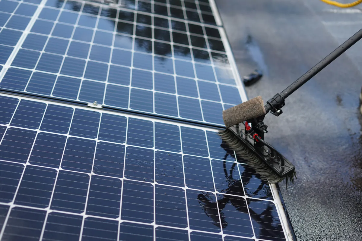 Long-handled soft brush washing a rooftop solar panel with water