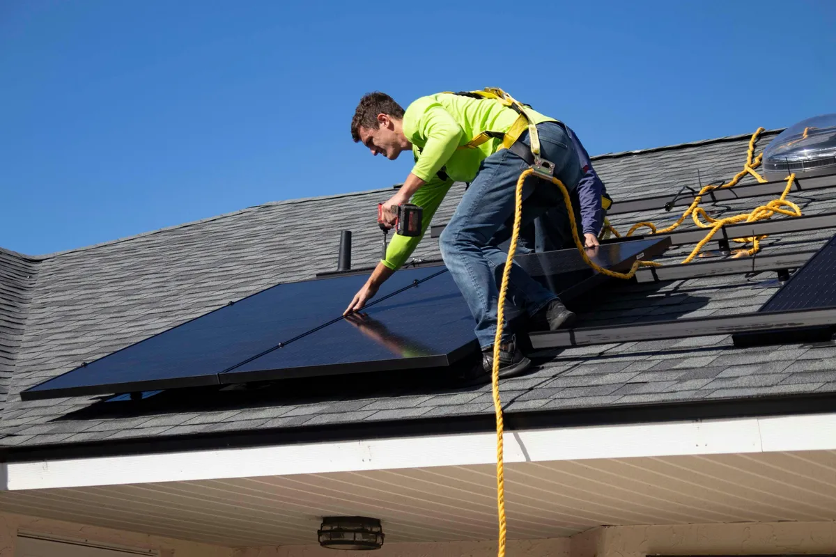 Harnessed technician servicing black solar panels on a residential shingle roof